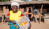 A Malawi woman smiling whilst holding a bread basket