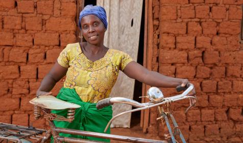 Aline Nibogora poses for a portrait photo outside her house with a bicycle she bought for being part of the VSLA programme, on August 2nd 2023 in Kayagoro village, Makamba, Burundi.
