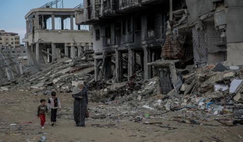 A family walks past buildings destroyed by missile strikes. Jalaa Street, Gaza City, 21 February 2024