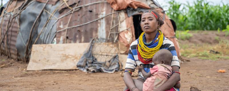 Woman kneels in front of hut