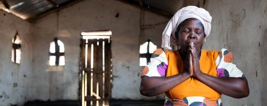 Esther sits in a church in a prayer pose with her eyes closed 