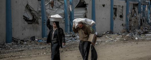 Man and woman carry supplies walking past buildings destroyed by missile strikes. Sina square, Gaza City, 21 February 2024